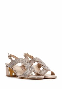 Sandales à talons beiges à lanières avec un talon carré, ornées de strass brillants et d'un design ondulé sur les lanières.