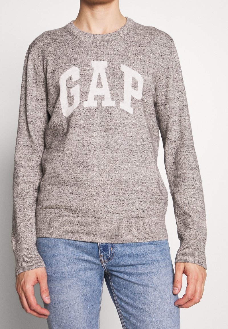 Grauer Strickpullover mit rundem Ausschnitt und langen Ärmeln, versehen mit dem „GAP“-Logo in hellbeige über der Brust. Strukturierter Stoff.