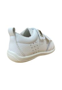 Zapatilla de cuero blanco con acabado texturizado, tira de velcro y pequeñas perforaciones. Suela de goma de color claro con un patrón de banda de rodadura.