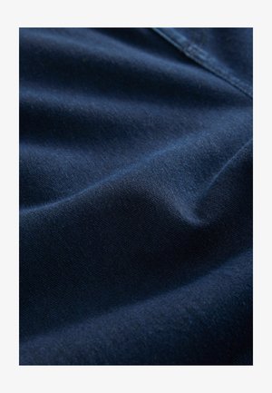 Tumma sininen kangas, jossa on pehmeä ja sileä pinta, hienovaraisia kiiltoja ja helläviä taitoksia, jotka ovat tyypillisiä puuvilla- tai farkkukankaalle.
