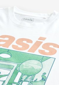 Vit bomullst-shirt med en stor orange "oasis"-grafik, med gröna illustrerade motiv av en cirkel och flamingosilhuetter.