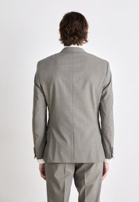 Blazer grigio e pantaloni abbinati con un discreto motivo a quadri. Il blazer presenta spalle strutturate e dettagli con bottoni sulle maniche.