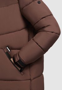 Rudos paduoto džemperio detalė, rodanti užtrauktuką turinčią kišenę, gana įtemptus rankogalius ir lygią tekstūrą su subtiliomis siūlėmis.