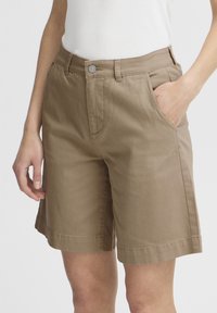 Shorts en coton beige à coupe droite, avec poches avant et fermeture par bouton. Le tissu a une texture lisse avec des coutures visibles.
