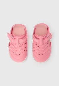 Ροζ λαστιχένια σανδάλια με κυματιστό σχέδιο, ιμάντα με βέλκρο και οπές για αερισμό, με λευκή σόλα και λεία υφή.