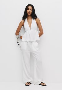 Bijela halter-top peplum bluzica uparena s labavim hlačama na vezanje. Tkanina izgleda lagano. Crne japanke upotpunjuju cjelokupni izgled.