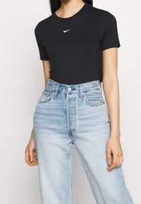 Svart kortärmad t-shirt med en vit Nike-logotyp, i kombination med ljusblå högmidjade denimjeans med en blekt textur och klassisk femfickdesign.