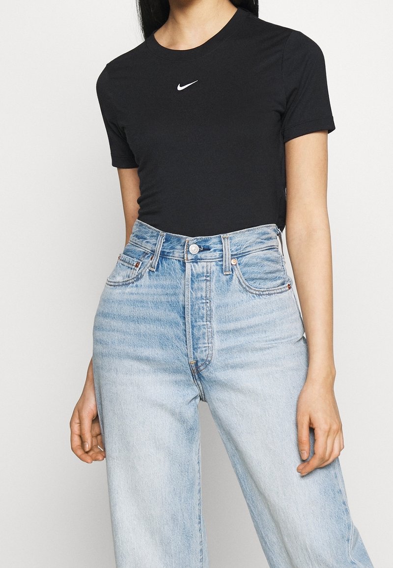 Svart kortärmad t-shirt med en vit Nike-logotyp, i kombination med ljusblå högmidjade denimjeans med en blekt textur och klassisk femfickdesign.