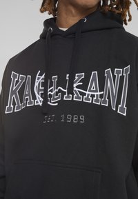 Felpa nera in cotone, con testo ricamato bianco "KALKANI" e "EST. 1989", dotata di tasca frontale e cordini sul cappuccio.