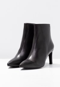 Stivaletti neri in pelle con punta affusolata e tacco alto sottile. Texture liscia, design elegante, con una silhouette minimalista.