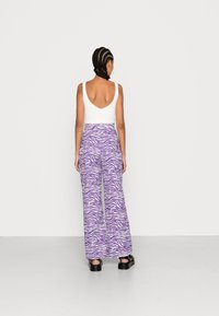 Calças largas de riscas zebra em roxo com uma cintura alta, combinadas com uma t-shirt justa branca. A textura parece suave com um design casual.