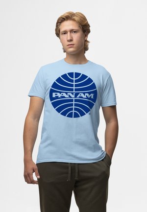 T-shirt en coton bleu clair avec un grand logo Pan Am bleu foncé dans un design circulaire. Manches courtes et col rond.