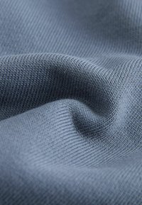 Tessuto a coste di un blu chiaro con una consistenza morbida, che mostra sottili linee verticali e pieghe dolci per dare profondità e movimento.