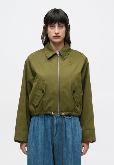 Veste courte couleur vert olive avec fermeture éclair frontale, grandes poches plaquées et ourlet à cordon. Comprend un col large et des manches structurées.