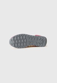 Sålen av en rosa sneakers som viser grå gummibane med trekantede mønstre og "Saucony"-logoen preget nær hælen.