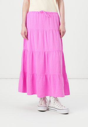 Gonna maxi rosa a strati realizzata in tessuto leggero, con una vita regolabile tramite cordino. Abbinata a sneakers bianche alte.