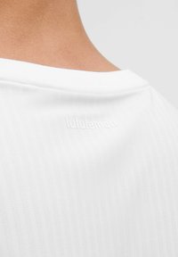 Valkoinen urheilupaita, jossa on pehmeä, teksturoitu kangas ja hienovarainen nukkakuvio; 'lululemon' -logo kohoilee takataskun kaula-aukossa.