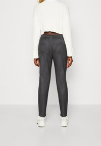 Graue Nadelstreifenhose mit schmalem Schnitt, ausgestattet mit einem elastischen Bund und Gesäßtaschen, kombiniert mit einem gekürzten weißen Pullover und Sneakers.