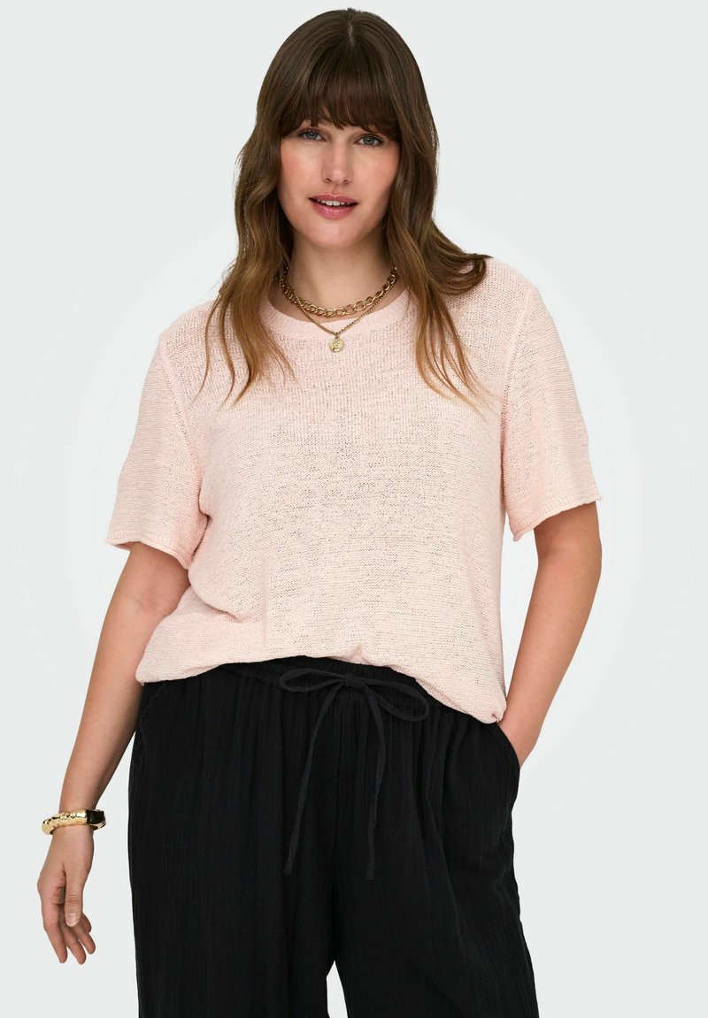 Šviesiai rožinė, trumpomis rankovėmis megzta palaidinė su laisvu siluetu, derinama su juodomis plisuotomis kelnėmis su raišteliu juosmenyje. Auksinė apyrankė kaip akcentas.