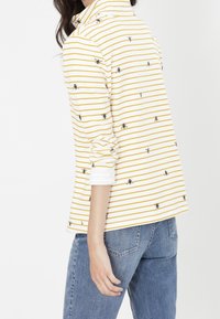Camisa de manga larga a rayas en blanco y amarillo con pequeños patrones de abejas negras; tejido suave, corte relajado, con puños enrollados; estilo casual.