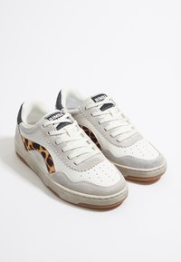 Zapatillas blancas y grises con acentos de estampado de leopardo, materiales de piel y ante texturizados, punta redonda, suela plana y un sistema de cordones sencillo.