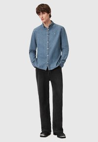 Lichtblauwe denim blouse met lange mouwen, gecombineerd met zwarte wijde broek. Opvallende accenten zijn witte knopen en een kraag.