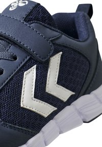 Baskets de sport bleu marine en mesh et en matériaux synthétiques, dotées d'une sangle Velcro, d'accents blancs et d'une semelle en caoutchouc transparent.