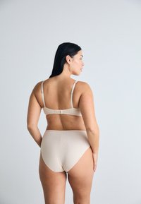 Beige naadloze beha en hoogzittende slipset. Verstelbare bandjes, haaksluiting op de beha, gladde textuur, minimalistisch ontwerp.