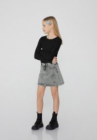 Haut noir à manches longues, jupe en denim grise avec des détails usés, et bottes de combat lacées noires. Accessoire pour les cheveux en bleu clair.