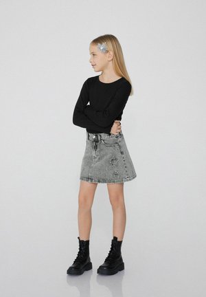 Haut noir à manches longues, jupe en denim grise avec des détails usés, et bottes de combat lacées noires. Accessoire pour les cheveux en bleu clair.