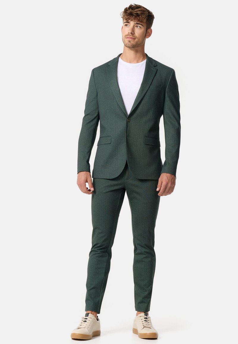 Grüner strukturierten Anzug mit geknöpftem Revers, tailliertem Design, kombiniert mit einem weißen T-Shirt und hellbeigen Sneakers. Verfügt über zwei Taschen auf dem Blazer.