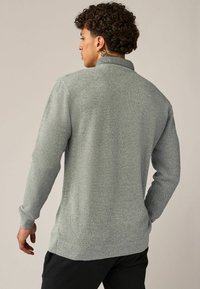 Pull en tricot gris avec une surface texturée, des poignets et un ourlet côtelés. Il présente un col. Couture visible et coupe décontractée.