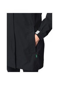 Giacca nera impermeabile con taglio dritto, tasche laterali con zip e un'etichetta sul polsino. Il materiale sembra liscio e resistente.