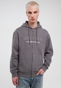 Grå zip-up hoodie lavet af blødt stof, med et logo-print foran, snore og en kengurulomme. Tekstureret finish med ribbede manchetter.