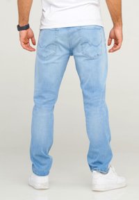 Jeans de mezclilla de color azul claro con corte recto, que cuentan con bolsillos traseros y detalles de costura. Combinados con zapatillas blancas.