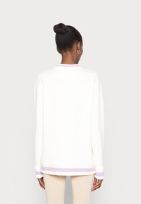 Sudadera blanca con cuello redondo, mangas largas y detalles en lila en los puños y el dobladillo. Textura suave y corte relajado.