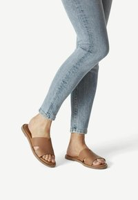 Sandales à glissière en cuir marron avec un bout ouvert et deux découpes ; semelle texturée ; portées avec un jean ajusté bleu clair.