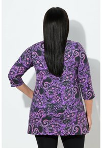 Fioletowa tunika w paisley z wzorem, z rękawami 3/4 i luźnym krojem, wykonana z miękkiej tkaniny, zestawiona z czarnymi legginsami.