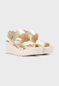 Sandalias de plataforma texturizadas en dorado con tiras onduladas, que presentan una suela blanca y un diseño abierto para mayor transpirabilidad y comodidad.