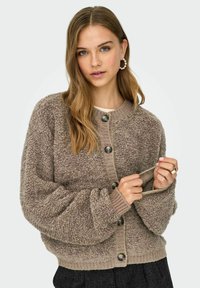 Puszysty kardigan w kolorze taupe z zaokrąglonym dołem, prążkowanymi mankietami i dużymi guzikami. Teksturowana tkanina o miękkim wyglądzie i luźnym kroju.