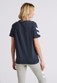 Mörkblå bomullst-shirt med korta ärmar och vita chevronränder på axlarna; avslappnad passform, slät textur, enkel design.