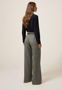 Blusa nera a maniche lunghe abbinata a pantaloni grigi a vita alta e gamba larga con dettaglio in vita cinturato e tessuto testurizzato.