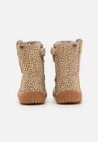Bottes en fausse fourrure avec un motif beige tacheté, dotées d'une surface texturée, d'une semelle en caoutchouc épaisse et de deux sangles à l'arrière pour un ajustement.