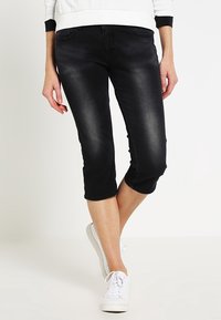 Vaqueros capri negros de mezclilla, con un ajuste entallado, ligero desgaste y longitud recortada, combinados con zapatillas blancas.