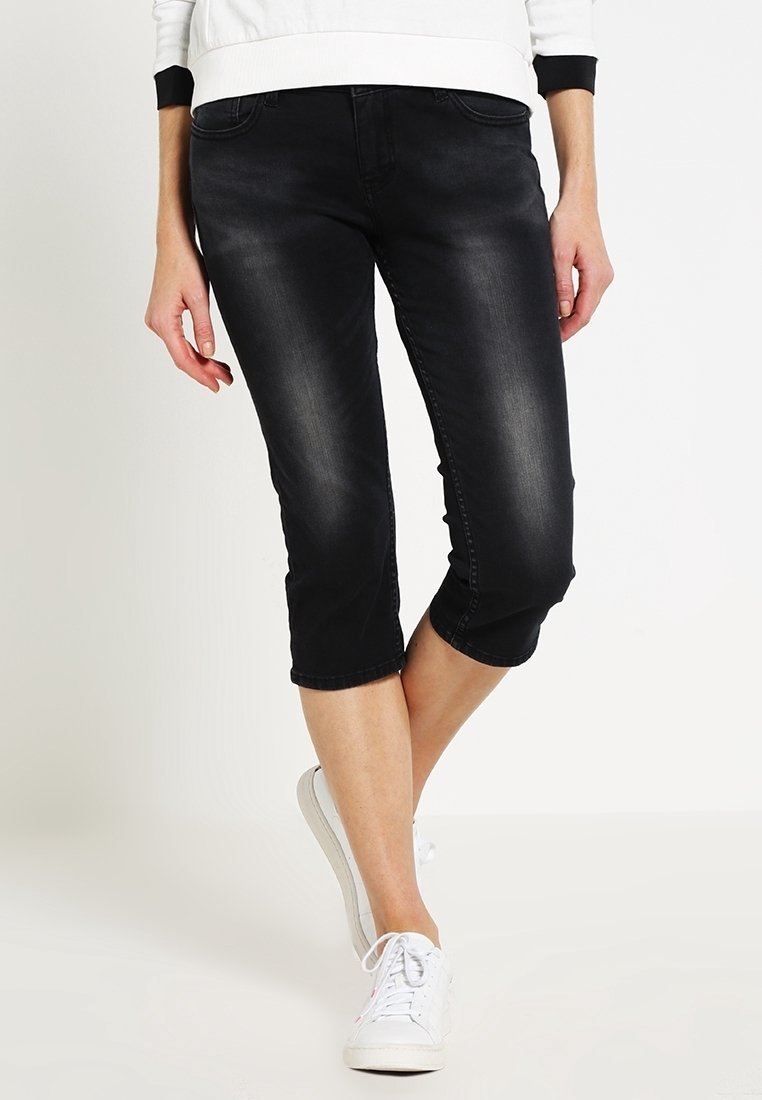 Vaqueros capri negros de mezclilla, con un ajuste entallado, ligero desgaste y longitud recortada, combinados con zapatillas blancas.