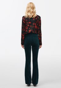 Zwarte bloes met bloemenprint, lange mouwen en een v-hals, gecombineerd met donkergroene flared corduroypants. Gladde textuur, aansluitende taille en zakken.