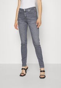 Jeans skinny de mezclilla gris con cintura media, bolsillos frontales y costuras visibles. Llevados con sandalias negras de tacón.