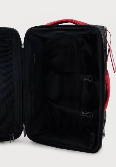 Ανοιχτή μαύρη βαλίτσα με κόκκινη λαβή, που διαθέτει εσωτερικούς ιμάντες συσκευασίας με αγκράφες και ένα τσεπάκι με φερμουάρ από δίχτυ στο καπάκι.