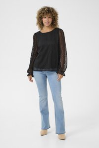 Black lace top with patterned texture and long puffed sleeves, paired with light blue flared jeans and beige footwear. Simple and elegant design.