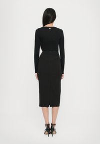 Zwarte lange mouwen top gecombineerd met een aansluitende zwarte midi rok met een split aan de achterkant en subtiele naaddetails. Strak, modern ontwerp.